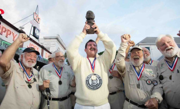 Surrounded by previous winners of the Hemingway Look-Alike Contest, 2026 champion Chris Dutton hoists his trophy, a bronze bust of Nobel Prize-winning author Ernest Hemingway, outside Sloppy Joe’s Bar.